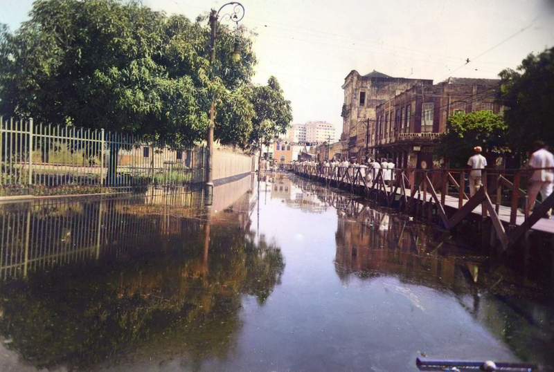 Em primeiro lugar, vista da rua Floriano Peixoto, em Manaus, com uma enchente pela cheia do rio Negro, em 1953, com as pontes de madeira construídas para a população transitar. Em segundo lugar, à esquerda, temos o gradil de ferro da Praça da Matriz. A água invadiu os prédios da Alfândega, da praça e dos estabelecimentos comerciais localizados na referida rua e adjacências. Foto: Silvino Santos.