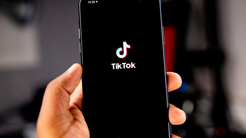 Mão segurando um celular com a logo do TikTok no meio da tela